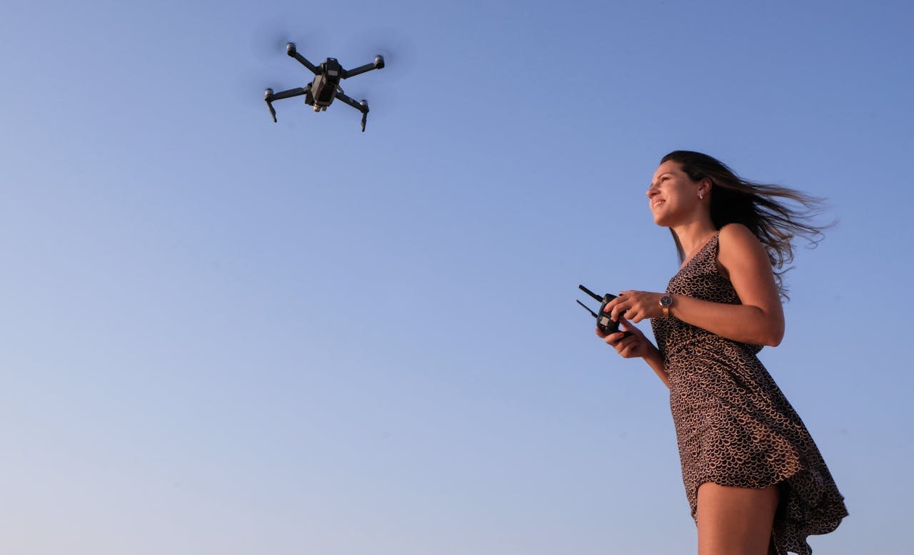 A woman enjoying flying a drone outdoors under a clear blue sky.